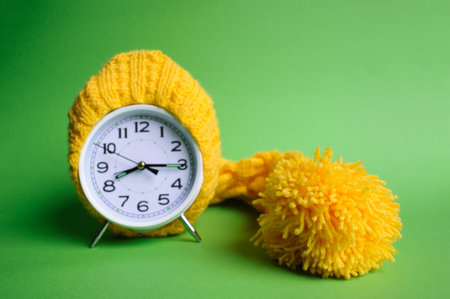 Alarm clock in yellow hat on the green background
