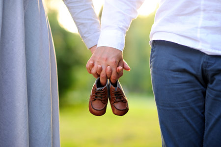 Happy and young pregnant couple with baby shoes in hands walking outdoorの写真素材