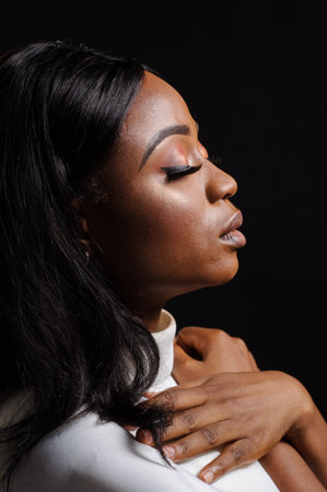 Portrait of a beautiful young African woman in white dress over black background. Studio pictureの写真素材