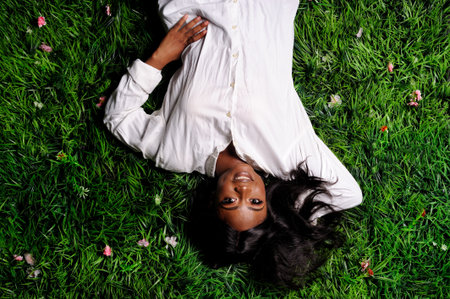 Portrait of beautiful african american woman laying on green grass in parkの写真素材