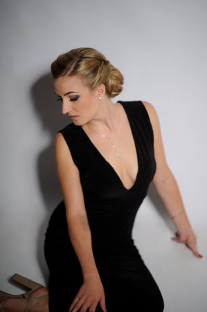 fashion picture of beautiful young blonde woman wearing black dress nice makeup. Studio picture, grey backgroundの写真素材