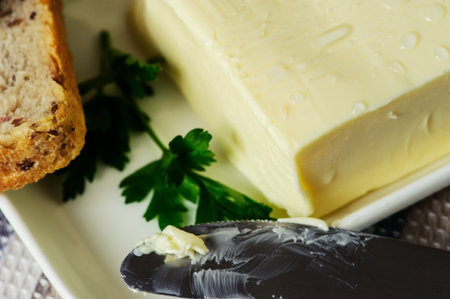 piece of butter with knife, bread and parsley on a wooden deskの写真素材