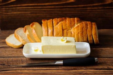 piece of butter with knife and bread on a wooden deskの写真素材