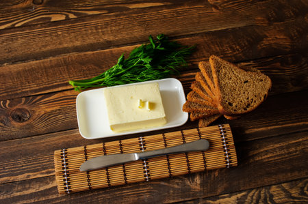 piece of butter with knife, bread and parsley on a wooden deskの写真素材