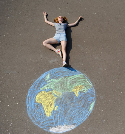 Schoolgirl on a chalk-drawn earth sphere on a asphaltの写真素材