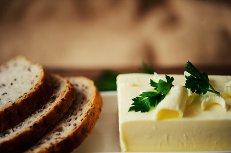 piece of butter with knife, bread and parsley on a wooden desk