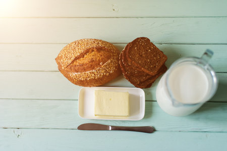 traditional bread loaf, butter and jug of milk on a lime wooden boardの写真素材