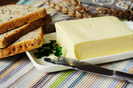 piece of butter with knife, bread and parsley on a wooden deskの写真素材