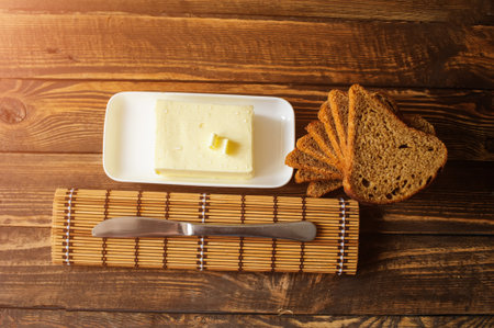 piece of butter with knife and bread on a wooden deskの写真素材