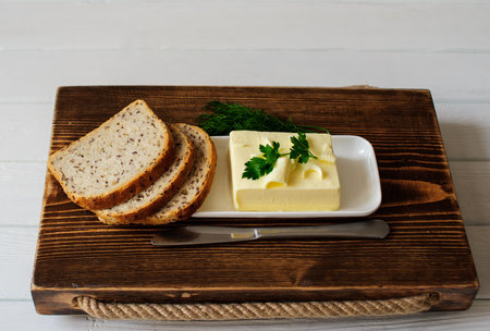 piece of butter with knife, bread and parsley on a wooden deskの写真素材