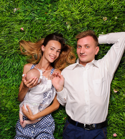 happy parents with newborn baby laying on the green grassの写真素材