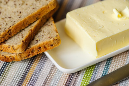 piece of butter with knife and bread on a wooden deskの写真素材