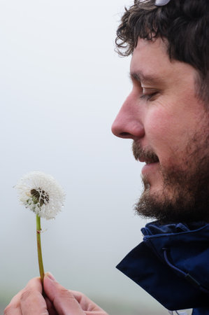 man holding dandelion with water drops in the hands and making a wish