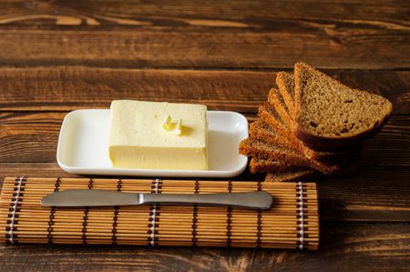 piece of butter with knife and bread on a wooden deskの写真素材