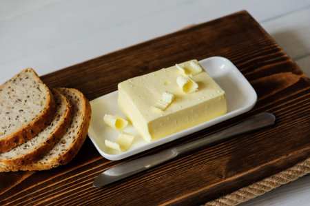 piece of butter with knife and bread on a wooden deskの写真素材