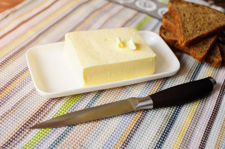 piece of butter with knife and bread on a wooden deskの写真素材