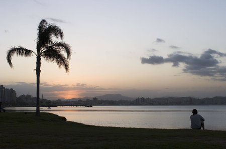 A young man contemplating the sunset on a tropical beach. Florianopolis - Santa Catarina - Brazil.の写真素材