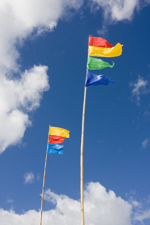 Colorful flags waving in the wind with blue sky and white clouds in the background