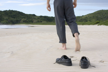 Businessman walking barefoot on a empty beach. Focus on his shoes in the foregroundの写真素材