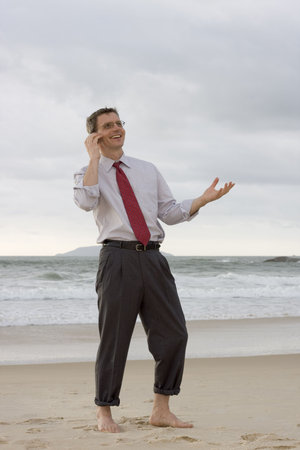 Businessman talking on cell phone while smiling and gesturing on a beachの写真素材