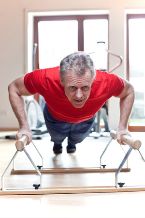 Mature man in red t-shirt doing push-ups in parallel bars in a gym
