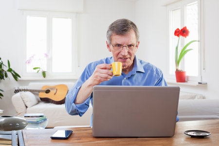 Senior or mature businessman drinking espresso in front of a computer in his home office - focus on...