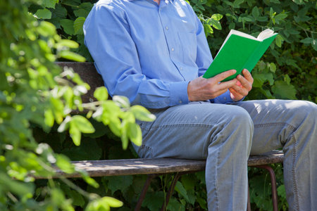 Relaxed businessman reading a green book on a park bench - focus on the green bookの写真素材