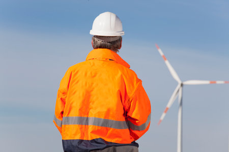 Worker or engineer with hard hat and protecive clothing looking at a windmill of a windfarm - focus on the manの写真素材
