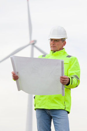 Mature engineer standing in front of a wind turbine with blueprint in his hand - focus on the faceの写真素材