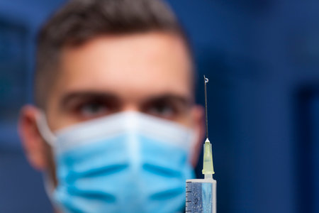 Close-up of doctor with medical mask preparing a syringe for vaccination against covid-19 - focus on the drop on the needleの写真素材