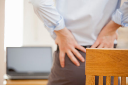 Businessman with backache standing in front of his workplace while working remotely from home -...