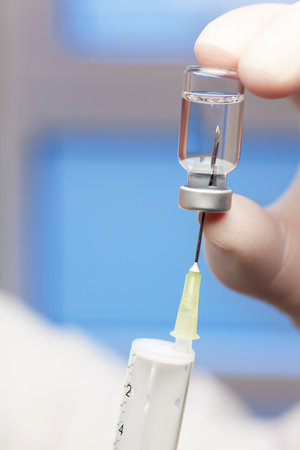 Extreme close-up of syringe and vaccine with fingers in surgical glove - focus on the needleの写真素材