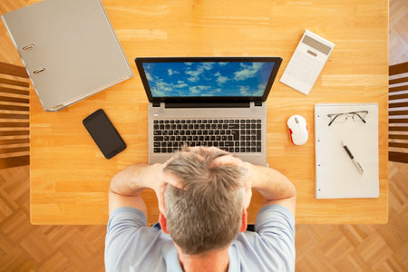 Stressed man sitting at a table with laptop while working from home - overhead view - the photo on the screen was taken by meの写真素材