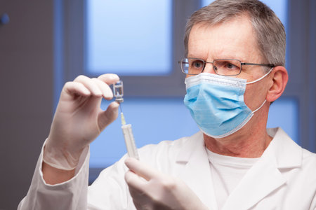 Doctor with medical mask preparing a syringe for vaccination against covid-19 - focus on the faceの写真素材