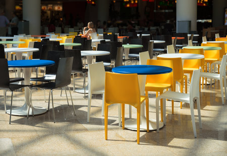 Different vibrant multicolor seats and desks in big public tavern hall area in retro style. Inside view with space for text on dark backdrop with lonely girl drinking juiceの写真素材