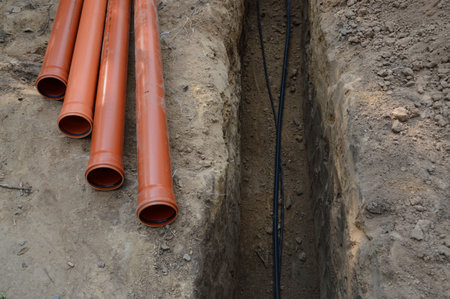 Safety supply to house new insulated internet, gas cord, red metal-plastic tap system construction lay in pit dug in garden. Top view with space for text on grey clay earth. Telecom service industryの写真素材