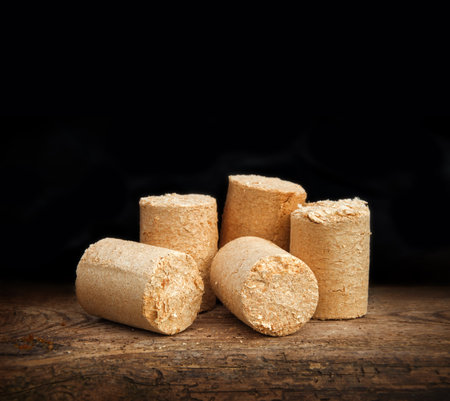 Heap of eco source of energy. Peat briquettes cylindrical form on old brown desk. Detail closeup view with space for text on dark backdropの写真素材