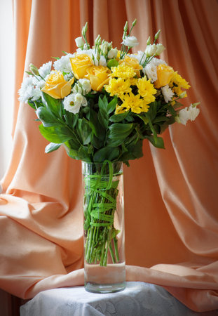 Beautiful large lush elegant vivid light orange color flowerheads in glassware flowerpot at golden curtains. View close-up with space for textの写真素材