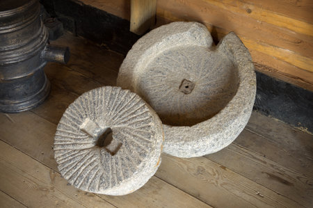 Mortar hewn aged grunge millwheel with handle and hole for processing seeds, fruits into farina powder, oil, spice for cooking. Close-up view with space for text on dark backdrop of wooden barnの写真素材