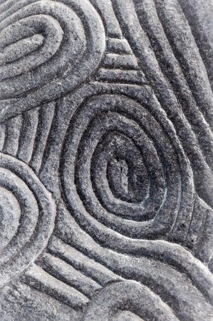 Design of naive round ethnic pagan intricacy motif in deep convex volume rough bumpy weathered furrow notch coarse wall slab. Close-up view with space for text on dark leaden stripesの写真素材
