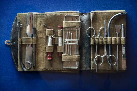 Aged nurse physician accessory in container on blue background. Aseptic hemostat, hypodermic tube, extraction tenaculum, steel hand lancet, tooth probe device, iron forcipes. Closeup obsolete objectの写真素材