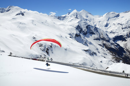 Alpen trip mountainside vista panorama of rock summit plateau scene. Bright blue heaven above tall crag. Wintertime sunlight scenic top view. Active athlete lifestyle. Person parasailing harness wingの写真素材