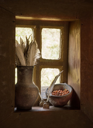 Antiquity scribe still life with goose pen in jar for write and dry ashberry in clay cup on wooden windowsill at dark hut. Closeup view with space for text in white glowing frame with glass backgroundの写真素材