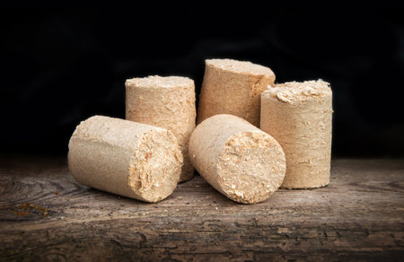 Eco source of energy. Peat briquettes cylindrical form on old brown desk. Detail closeup view with space for text on dark backdropの写真素材