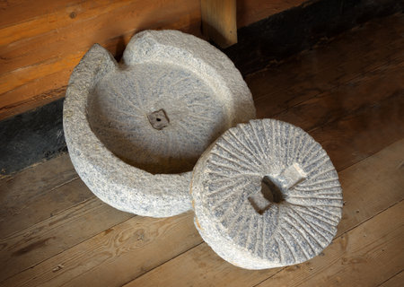 Mortar hewn aged grunge millwheel with handle and hole for processing seeds, fruits into farina powder, oil, spice for cooking. Close-up view with space for text on dark backdrop of wooden barnの写真素材