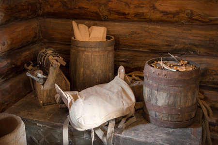 Grungy aged country style storage used oak tun barel, worn horse seat, supply items making store on dusty chest in board shed. Closeup view with space for text on dark brown bar wall cottage backdropの写真素材