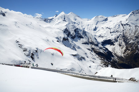 Alpen trip mountainside vista panorama of rock summit plateau scene. Bright blue heaven above tall crag. Wintertime sunlight scenic top view. Active athlete lifestyle. Person parasailing harness wingの写真素材