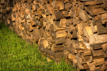Picturesque old yellow billets stacked high logstack wall loaded on green grass lit by bright evening summer warm sun. View close-up with space for text on garden lawnの写真素材