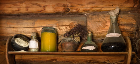 Grunge storage cupboard in hut with corked ink vial, poison phial, dry herb bunch, oil, scattered flour, jam and liqueur in jug with label for title. Closeup view with space for text on brown bar wallの写真素材