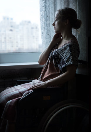 Pretty adult alone headache lady patient seat in hospital room look on light white city copyspace. Paralysis loss teen human lifestyle concept with space for text on gloomy dark home indoor backgroundの写真素材